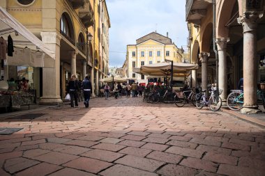 Mantova, İtalya - 8 Mart 2025 - Pazar tezgahları ve bulutlu bir günde kafelerin yanından geçen insanlar