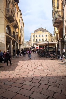 Mantova, İtalya - 8 Mart 2025 - Pazar tezgahları ve bulutlu bir günde kafelerin yanından geçen insanlar