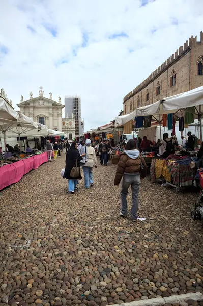 Mantova, İtalya - 8. Mart 2025 - Arka planda bir kilise olan bir sarayın ve insanların market tezgahlarına göz attığı bir meydanın yanındaki kaldırımlı meydan