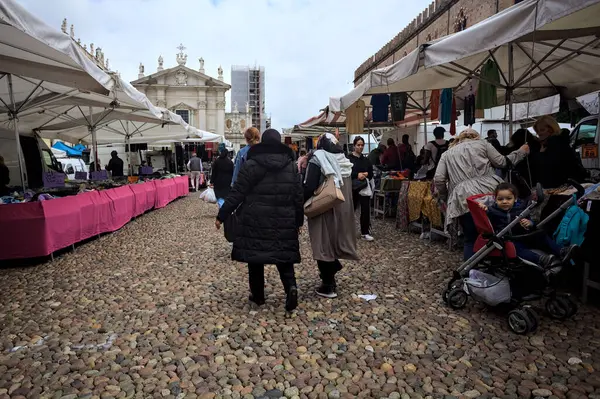 Mantova, İtalya - 8. Mart 2025 - Arka planda bir kilise olan bir sarayın ve insanların market tezgahlarına göz attığı bir meydanın yanındaki kaldırımlı meydan