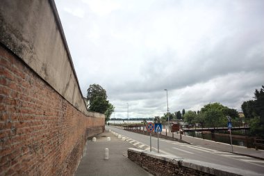 İtalya 'da bulutlu bir günde göl kıyısında tuğla bir duvarın yanındaki yol.