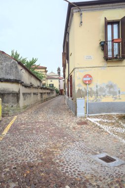 Bulutlu bir günde, İtalya 'da küçük bir binayla bir sınır duvarının arasından geçen kaldırımlı bir cadde.