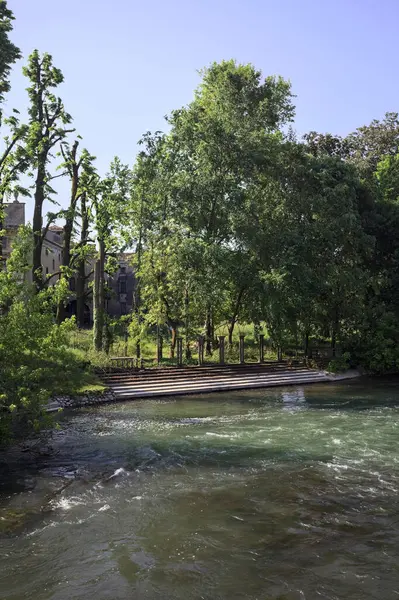 İtalya kırsalındaki nehir kıyısındaki bir malikanenin bahçesindeki merdivenler uzaktan görülüyor.
