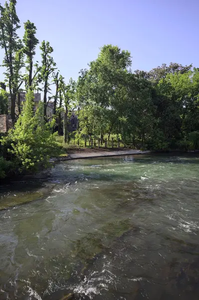 İtalya kırsalındaki nehir kıyısındaki bir malikanenin bahçesindeki merdivenler uzaktan görülüyor.