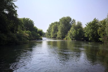 İtalya kırsalındaki bir parktan geçen nehir kıyıdaki ağaçlar ve bitkiler tarafından çerçevelenmiş bir şelale ile.