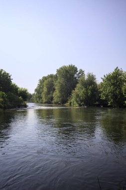 İtalya kırsalındaki bir parktan geçen nehir kıyıdaki ağaçlar ve bitkiler tarafından çerçevelenmiş bir şelale ile.