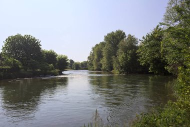 İtalya kırsalındaki bir parktan geçen nehir kıyıdaki ağaçlar ve bitkiler tarafından çerçevelenmiş bir şelale ile.