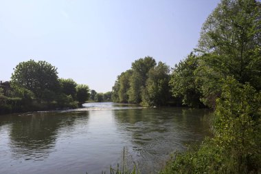 İtalya kırsalındaki bir parktan geçen nehir kıyıdaki ağaçlar ve bitkiler tarafından çerçevelenmiş bir şelale ile.