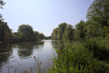 İtalya kırsalındaki bir parktan geçen nehir kıyıdaki ağaçlar ve bitkiler tarafından çerçevelenmiş bir şelale ile.