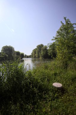 İtalya kırsalındaki bir parktan geçen nehir kıyıdaki ağaçlar ve bitkiler tarafından çerçevelenmiş bir şelale ile.