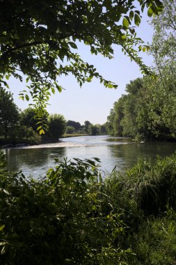 İtalya kırsalındaki bir parktan geçen nehir kıyıdaki ağaçlar ve bitkiler tarafından çerçevelenmiş bir şelale ile.