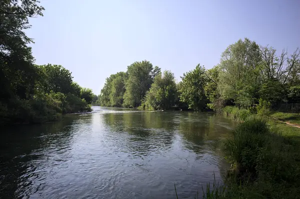 İtalya kırsalındaki bir parktan geçen nehir kıyıdaki ağaçlar ve bitkiler tarafından çerçevelenmiş bir şelale ile.