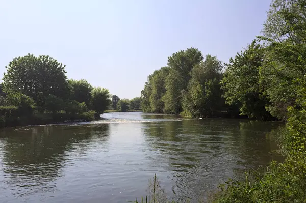İtalya kırsalındaki bir parktan geçen nehir kıyıdaki ağaçlar ve bitkiler tarafından çerçevelenmiş bir şelale ile.