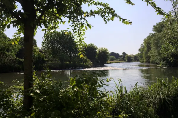 İtalya kırsalındaki bir parktan geçen nehir kıyıdaki ağaçlar ve bitkiler tarafından çerçevelenmiş bir şelale ile.