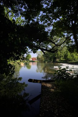 İtalya kırsalındaki bir parkta, üzerinde şelale olan bir nehirde kıvrıl. Gölgedeki ağaçlarla çerçevelenmiş.