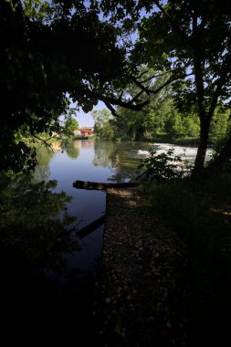 İtalya kırsalındaki bir parkta, üzerinde şelale olan bir nehirde kıvrıl. Gölgedeki ağaçlarla çerçevelenmiş.