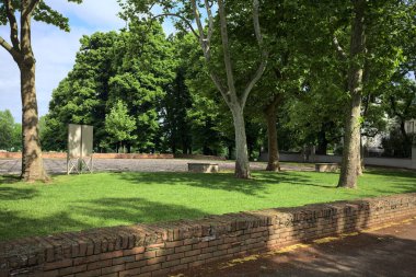 İtalya 'da güneşli bir günde ağaçların çerçevelediği bir parkta bir açıklığın kenarında taş bir bank.