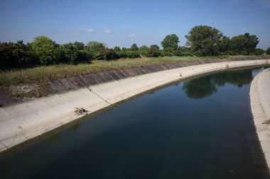 İtalya kırsalında ağaçlarla çevrili bir alanın yanındaki saptırıcı kanal.