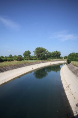 İtalya kırsalında ağaçlarla çevrili bir alanın yanındaki saptırıcı kanal.