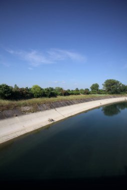 İtalya kırsalında ağaçlarla çevrili bir alanın yanındaki saptırıcı kanal.