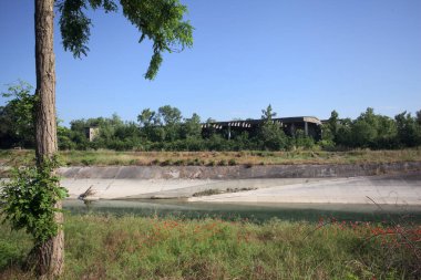 Bir ağaç tarafından çerçevelenmiş güneşli bir günde İtalya kırsalında bir eğlence kanalı.