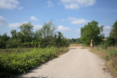 İtalya 'nın kırsal kesimlerinde güneşli bir günde bir bar tarafından engellenmiş, üzerinde elektrik hattı olan tarlalar arasındaki kirli yol.