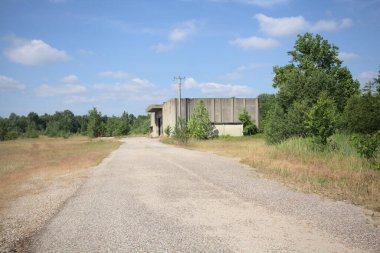 Terk edilmiş bir depo ve önünde çıplak bir avludan görünen asfaltlı bir giriş yolu var.