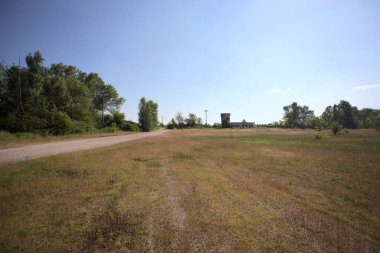 Çamur yolu, güneşli bir günde kuru çimenler ve ağaçlarla kaplı bir bahçenin yanındaki paslı bir bar tarafından kapatıldı.