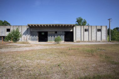 Terk edilmiş bir yerleşkenin depoları güneşli bir günde ağaçlarla çevrili İtalya kırsalında kuru çimenler ve çakıllarla çevrili bir bahçeden görülebiliyor.