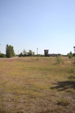 Çamur yolu, güneşli bir günde kuru çimenler ve ağaçlarla kaplı bir bahçenin yanındaki paslı bir bar tarafından kapatıldı.