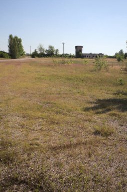 Çamur yolu, güneşli bir günde kuru çimenler ve ağaçlarla kaplı bir bahçenin yanındaki paslı bir bar tarafından kapatıldı.
