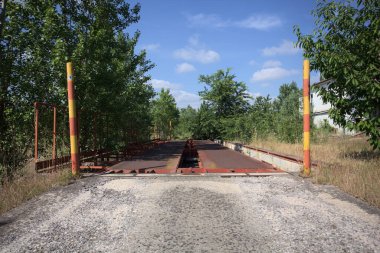 Güneşli bir günde terk edilmiş bir endüstriyel tesiste çalılarla çevrili bir ölçek platformu.