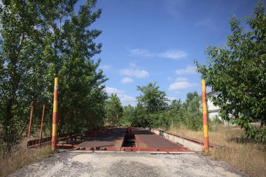 Güneşli bir günde terk edilmiş bir endüstriyel tesiste çalılarla çevrili bir ölçek platformu.