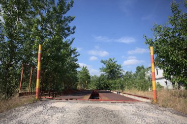 Güneşli bir günde terk edilmiş bir endüstriyel tesiste çalılarla çevrili bir ölçek platformu.