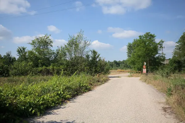 İtalya 'nın kırsal kesimlerinde güneşli bir günde bir bar tarafından engellenmiş, üzerinde elektrik hattı olan tarlalar arasındaki kirli yol.