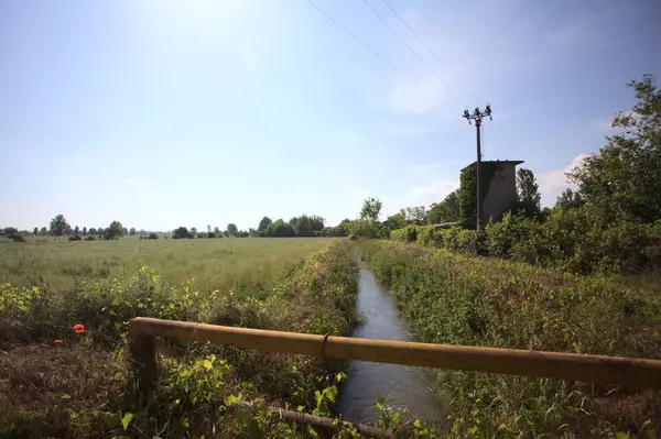 İtalya kırsalında terk edilmiş bir yerleşkenin kenarındaki çukur üzerinde gelincikler yetişen paslı bir trabzanın arkasından görülüyor.