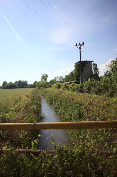 İtalya kırsalında terk edilmiş bir yerleşkenin kenarındaki çukur üzerinde gelincikler yetişen paslı bir trabzanın arkasından görülüyor.