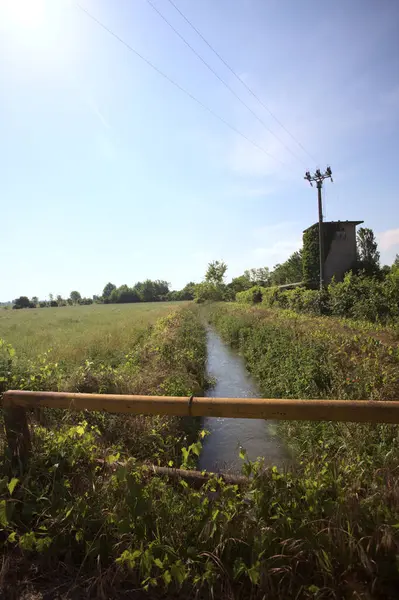İtalya kırsalında terk edilmiş bir yerleşkenin kenarındaki çukur üzerinde gelincikler yetişen paslı bir trabzanın arkasından görülüyor.