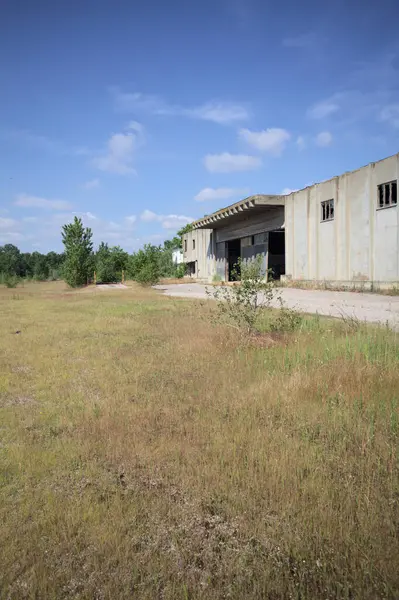Terk edilmiş bir depo ve önünde çıplak bir avludan görünen asfaltlı bir giriş yolu var.