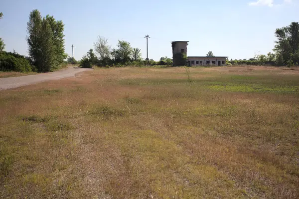 Çamur yolu, güneşli bir günde kuru çimenler ve ağaçlarla kaplı bir bahçenin yanındaki paslı bir bar tarafından kapatıldı.