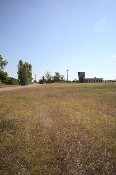 Çamur yolu, güneşli bir günde kuru çimenler ve ağaçlarla kaplı bir bahçenin yanındaki paslı bir bar tarafından kapatıldı.