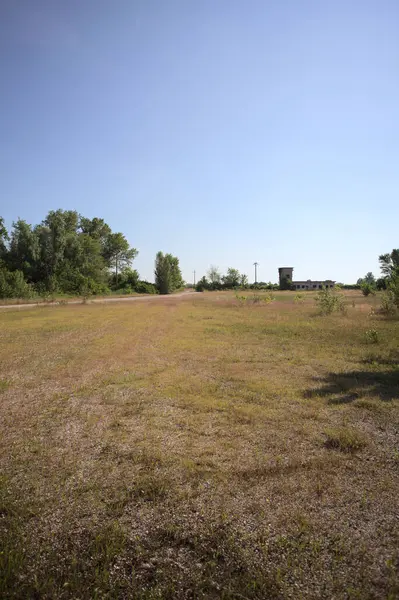 Çamur yolu, güneşli bir günde kuru çimenler ve ağaçlarla kaplı bir bahçenin yanındaki paslı bir bar tarafından kapatıldı.