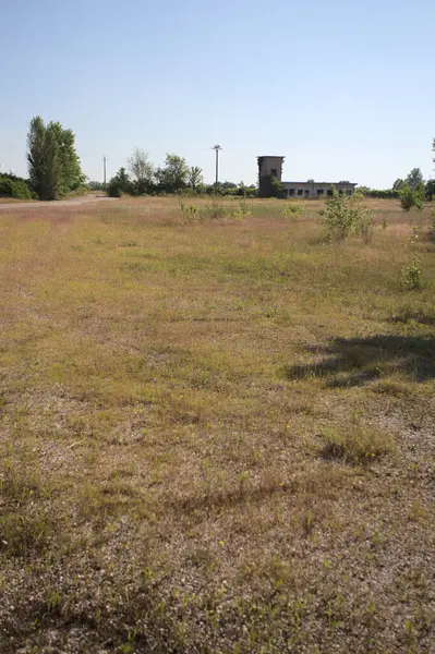 Çamur yolu, güneşli bir günde kuru çimenler ve ağaçlarla kaplı bir bahçenin yanındaki paslı bir bar tarafından kapatıldı.