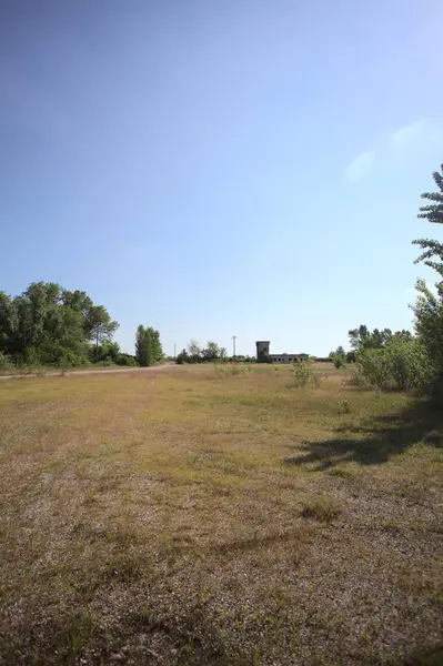 Çamur yolu, güneşli bir günde kuru çimenler ve ağaçlarla kaplı bir bahçenin yanındaki paslı bir bar tarafından kapatıldı.