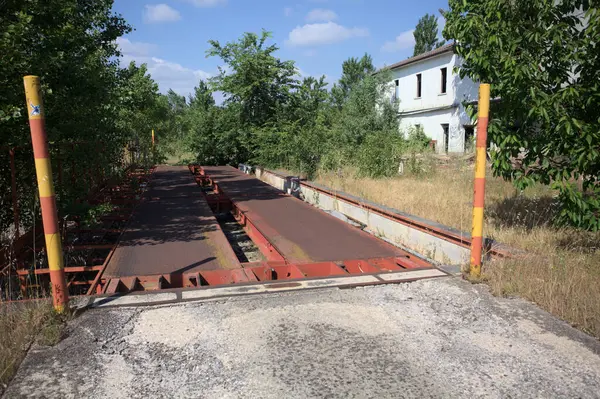 Güneşli bir günde terk edilmiş bir endüstriyel tesiste çalılarla çevrili bir ölçek platformu.