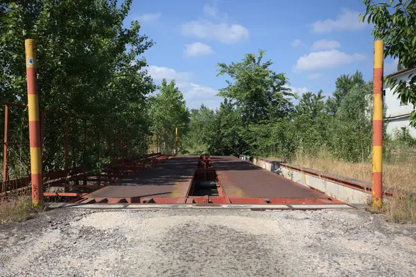Güneşli bir günde terk edilmiş bir endüstriyel tesiste çalılarla çevrili bir ölçek platformu.