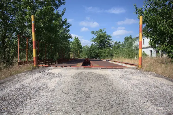Güneşli bir günde terk edilmiş bir endüstriyel tesiste çalılarla çevrili bir ölçek platformu.