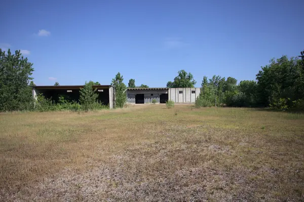 Terk edilmiş bir yerleşkenin depoları güneşli bir günde ağaçlarla çevrili İtalya kırsalında kuru çimenler ve çakıllarla çevrili bir bahçeden görülebiliyor.