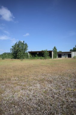 Terk edilmiş bir yerleşkenin depoları güneşli bir günde ağaçlarla çevrili İtalya kırsalında kuru çimenler ve çakıllarla çevrili bir bahçeden görülebiliyor.