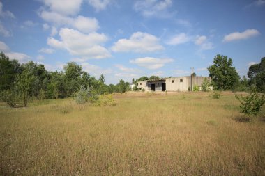 Terk edilmiş bir yerleşkenin depoları güneşli bir günde ağaçlarla çevrili İtalya kırsalında kuru çimenler ve çakıllarla çevrili bir bahçeden görülebiliyor.